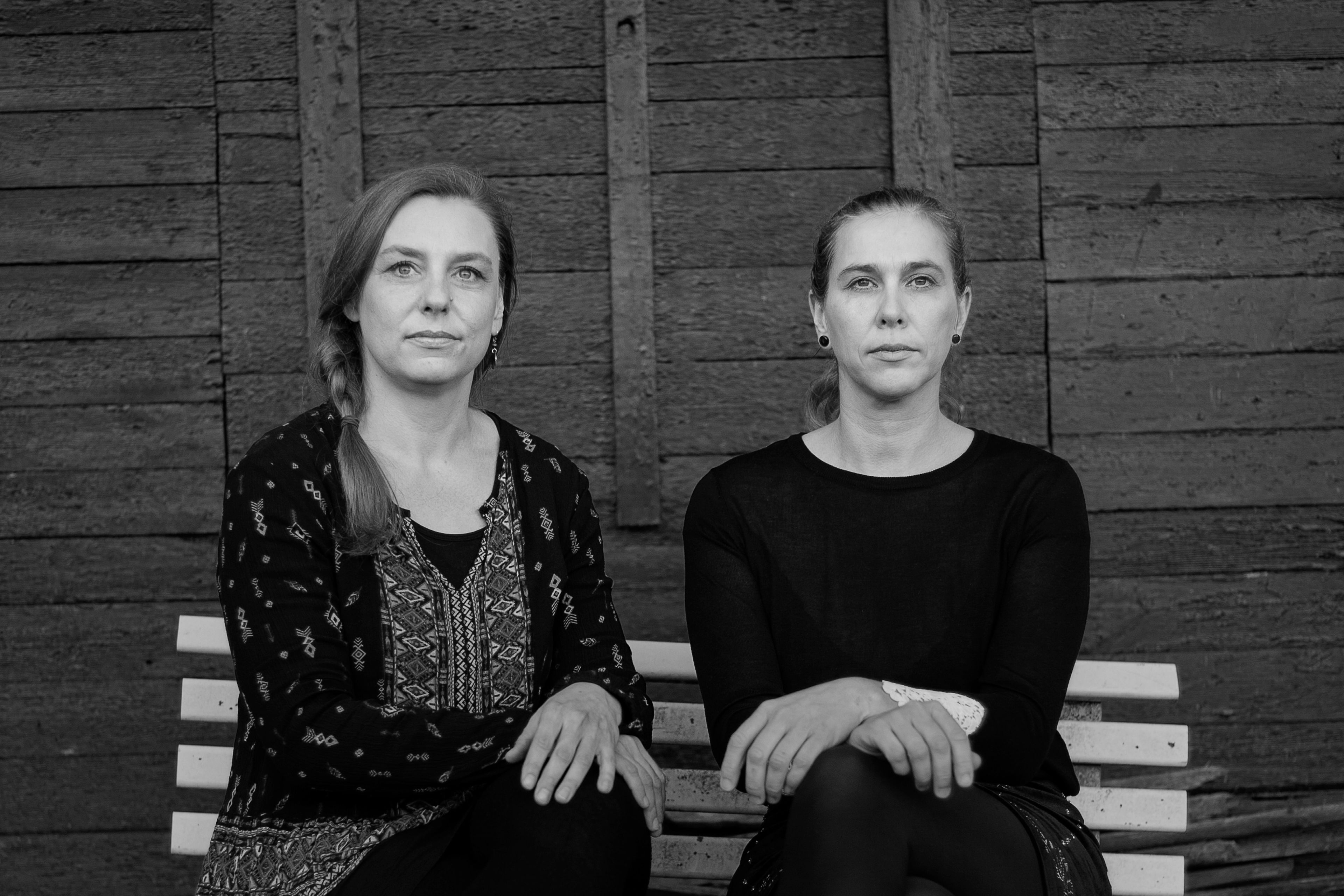 Lena und Jenny sitzen auf einer Bank vor einer Holzwand schwarzweiss